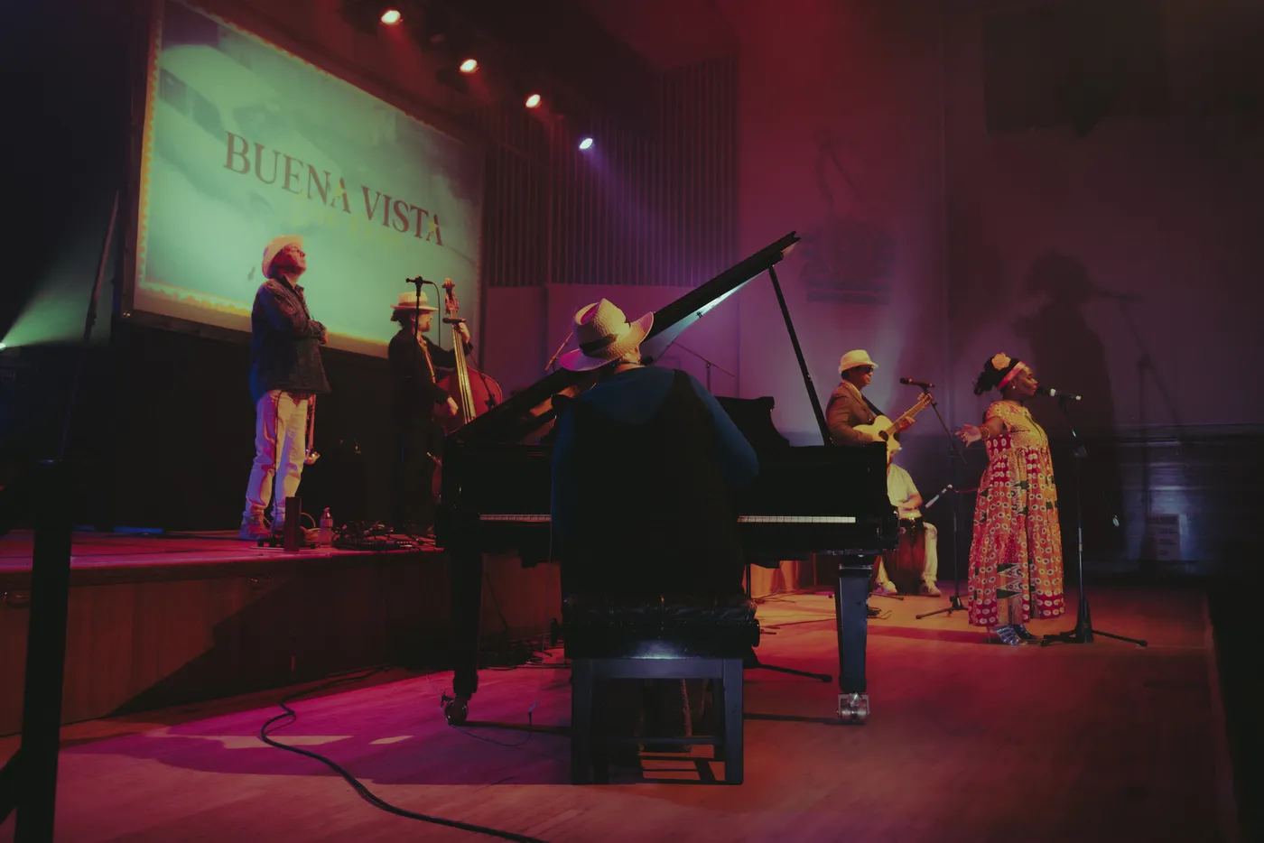 The band on stage seen from behind the grand piano, with a singer in a patterned dress on the right