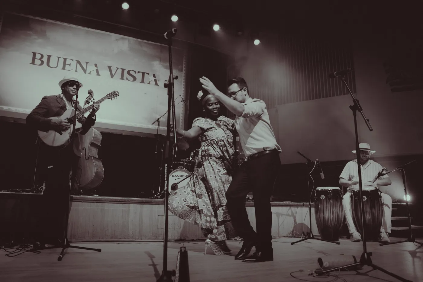 Black and white photograph of two performers dancing on stage while a guitarist and a conga player play