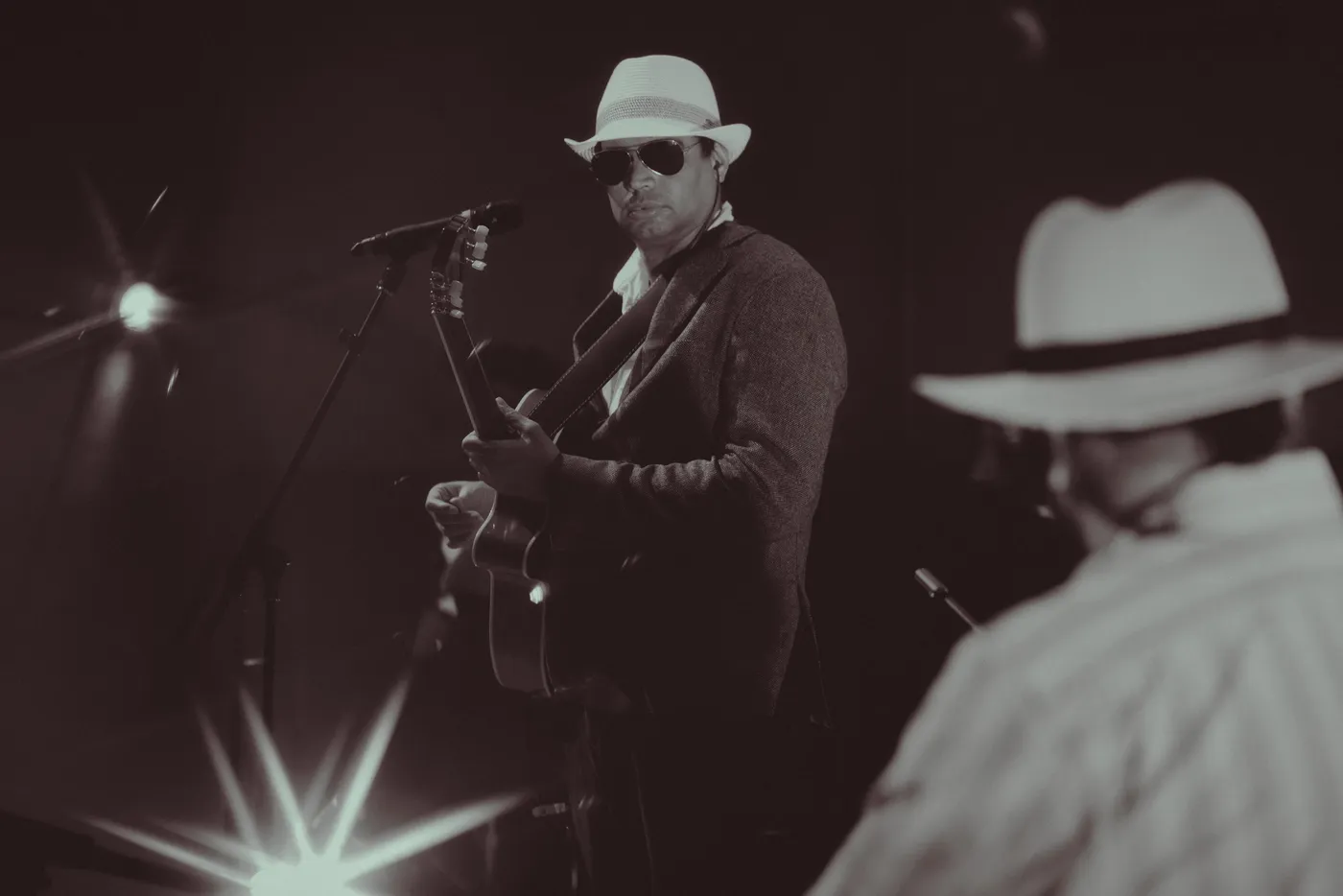 Black and white photograph of a guitarist in a white hat and sunglasses playing on stage