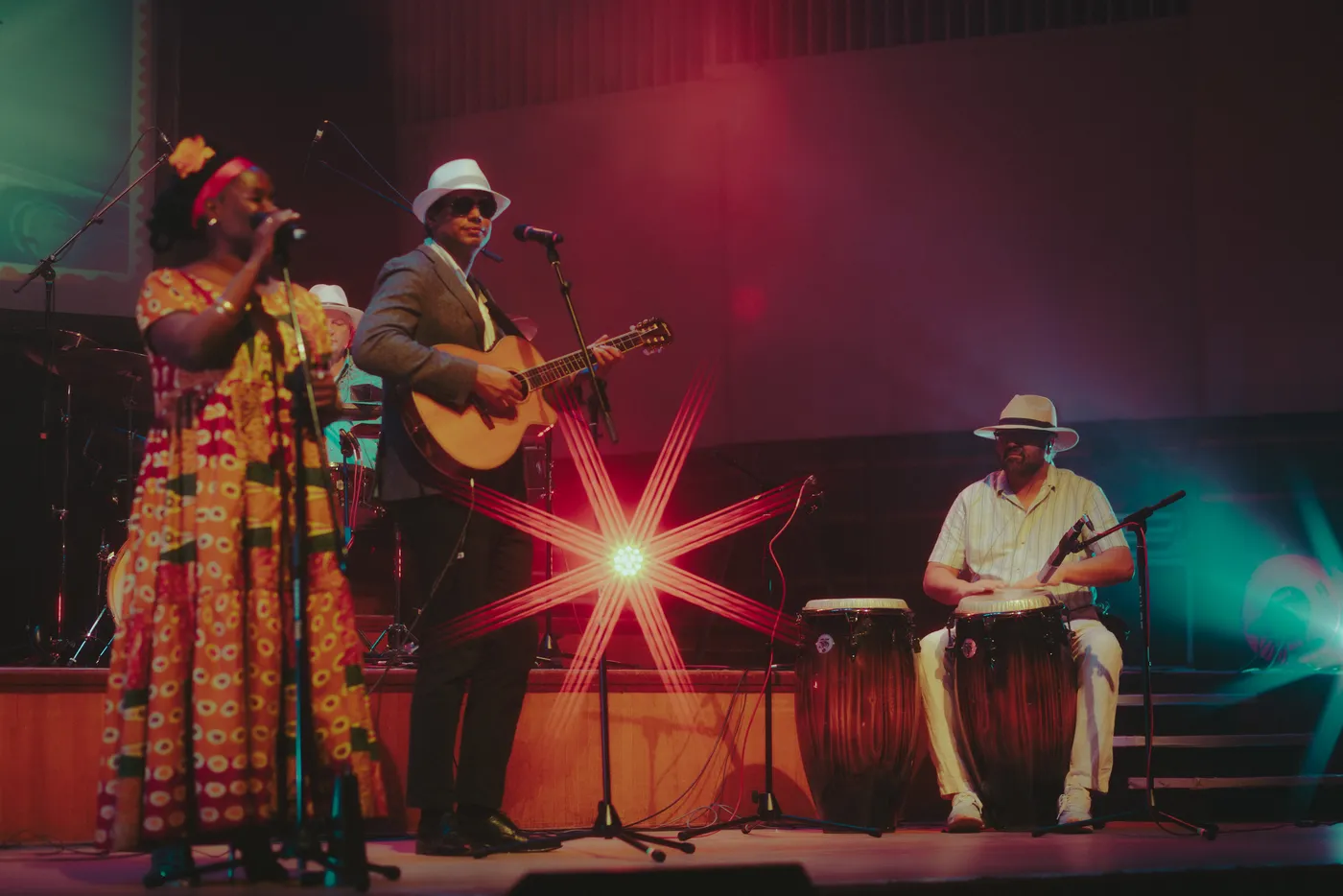 A singer and a guitarist in white hats sharing the front of the stage, with a conga player to the right