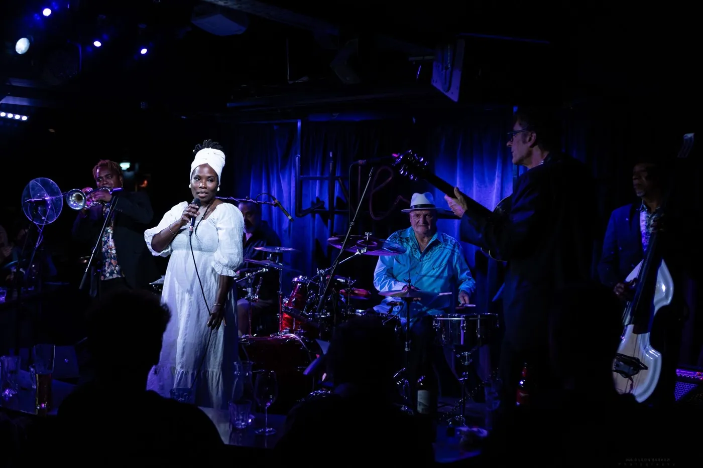 Buena Vista Live performing on a small club stage under blue light, with a trumpet, drums and a singer in white