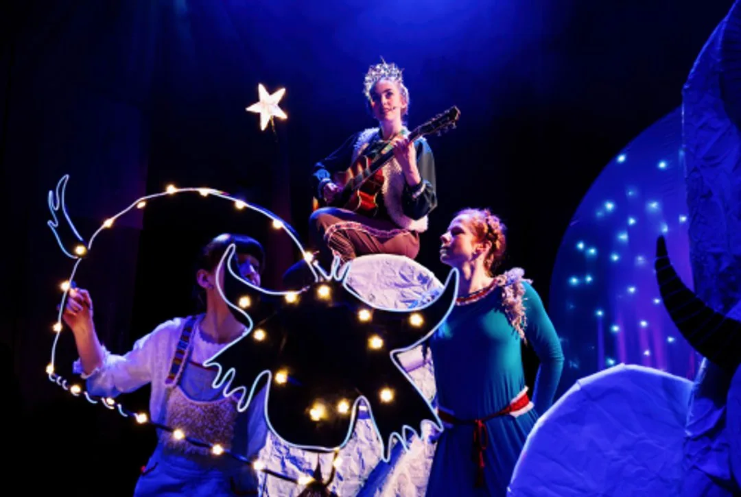 Performers stand behind a row of yak puppets in striped and knitted hats on a snowy stage set