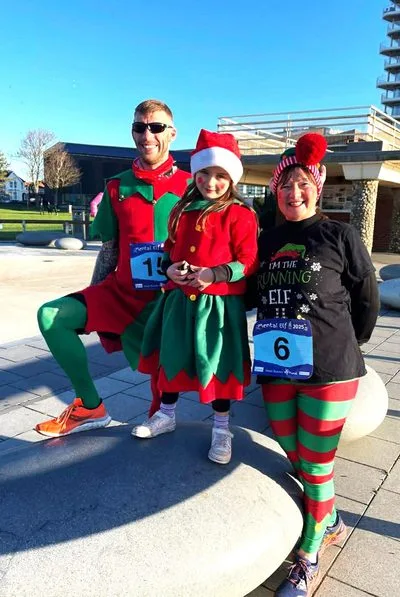 Three people in elf and Santa costumes wearing race numbers on Worthing seafront