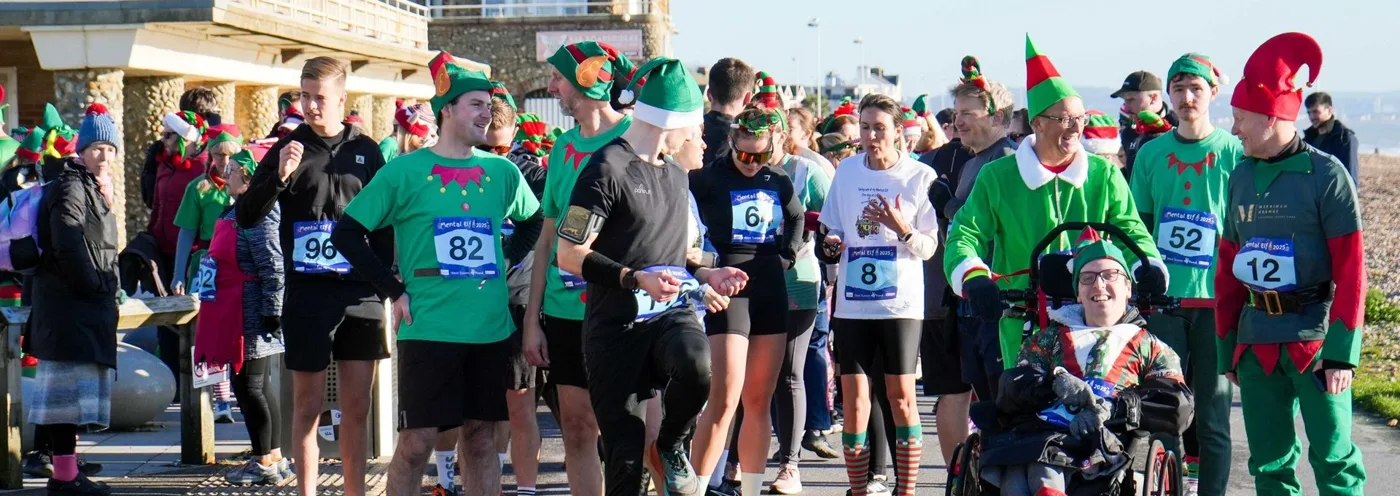 Runners in elf costumes and race numbers, with a wheelchair user, on Worthing seafront