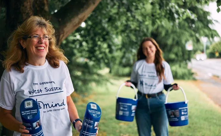 Two West Sussex Mind supporters in charity T-shirts holding collection buckets
