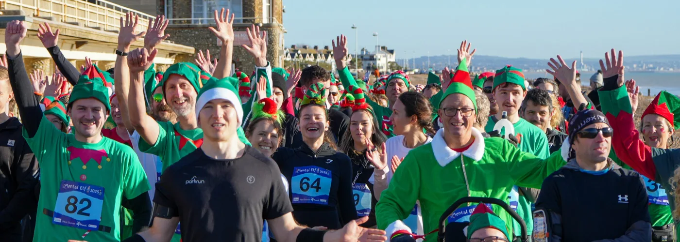 Elf-costumed runners and walkers wave before the start of the 2025 Mental Elf fun run on Worthing seafront.
