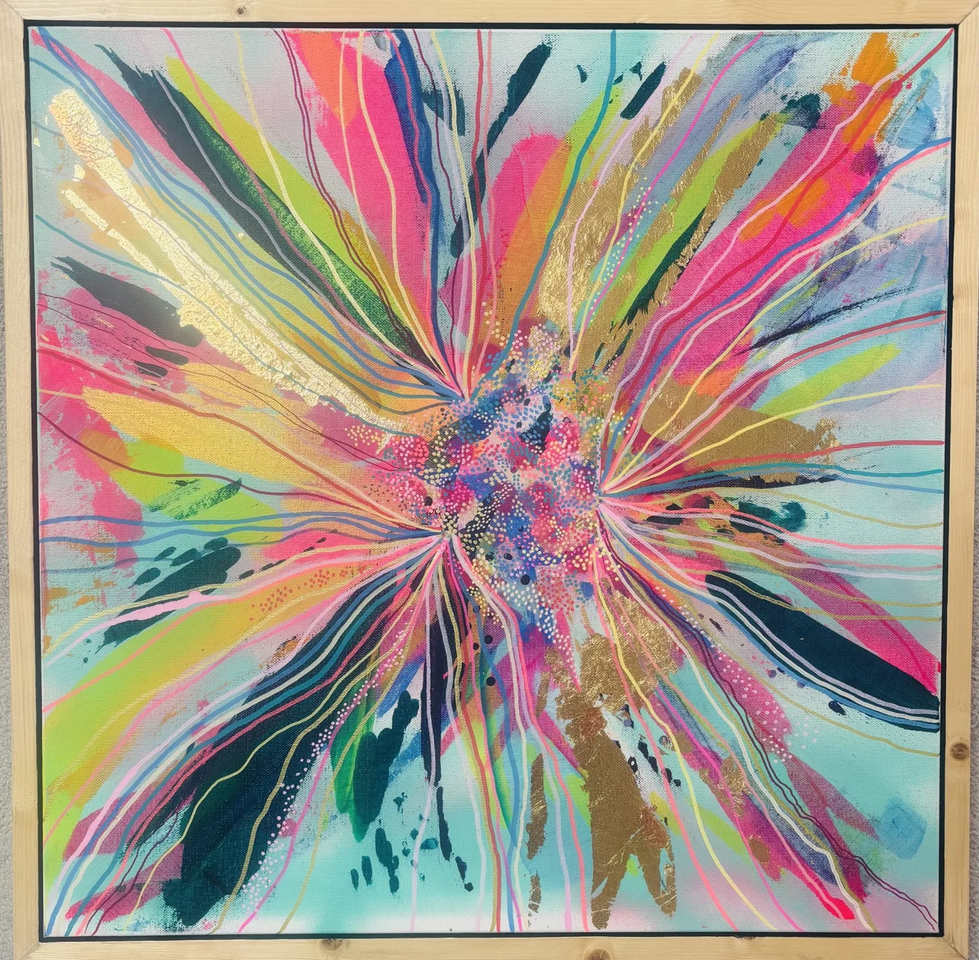 A square abstract flower painting in a pale wooden frame, with pink, lime, teal and gold-leaf strokes bursting out from a dotted centre